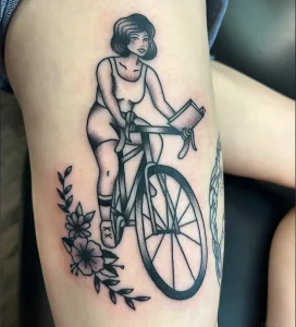 Черно-белая татуировка девушки в стиле ретро, едущей на старинном велосипеде с букетом цветов внизу