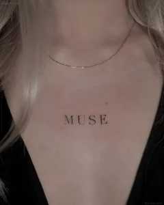 Крупный план женской груди с тонкой татуировкой надписью MUSE, выполненной в стиле минимализм