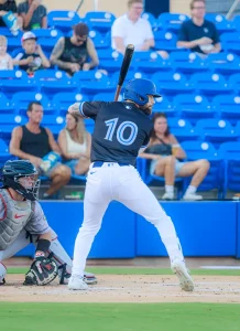 Игрок бейсбольного клуба Toronto Blue Jays Нэтан Льюкс в форме с номером 10 готовится к удару. На его правой руке, выставленной вперед, видна татуировка.