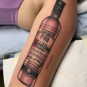 Детальная цветная татуировка бутылки водки Ketel One в стиле реализм на бедре девушки, выполненная с высокой проработкой этикетки и бликов