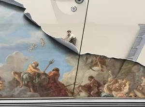Крупный план татуировки в стиле микро-реализм на кузове автомобиля Ford Mustang 1967 года. Изображение представляет собой фрагмент классической картины с фигурами богов и ангелами, выполненный тату-мастером Kozo.
