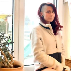 Женщина с дерзкой тату-моделью, демонстрирующая уникальную внешность и стиль на фоне окна.