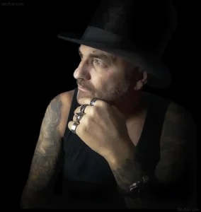 Мужчина с татуировками на руках и шее, позирующий для фотосессии в стиле гранж, демонстрируя уникальную эстетику тела.