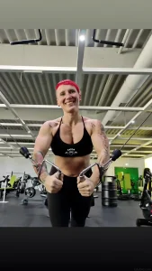Модель с ярко-красными волосами и татуировками на руках использует тренажер в зале, демонстрируя силуэт и уверенность.