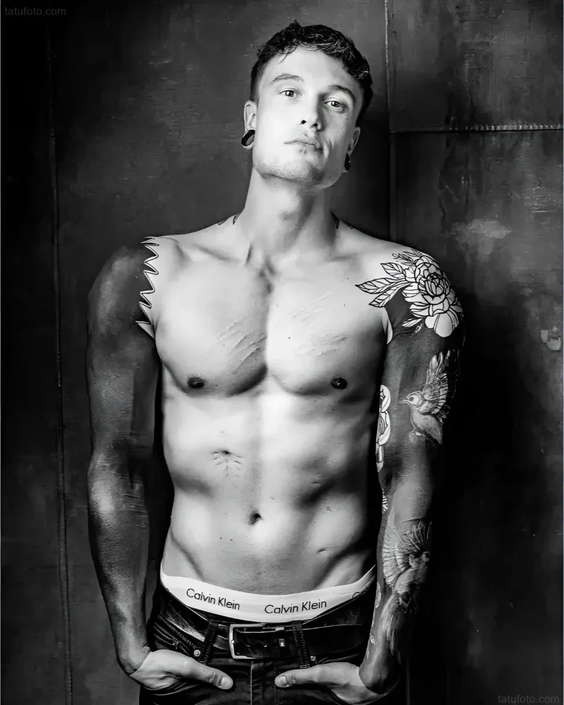 Mann mit Tätowierungen an Armen und Brust, der für eine Fotosession im Calvin Klein Stil posiert
