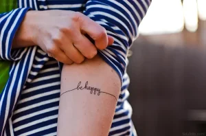 Поврежденное тату с надписью Be Happy на предплечье
