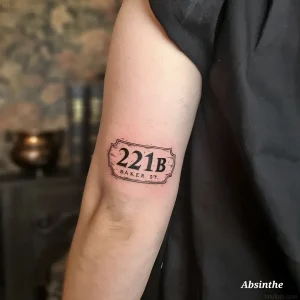 Татуировка с адресом "221B Baker Street" на руке человека, выполненная в стиле минимализма.