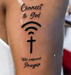 Черно-белая татуировка на коже с текстом Connect to God, символом Wi-Fi, где вместо точки — крест, и надписью Wifi password: Prayer