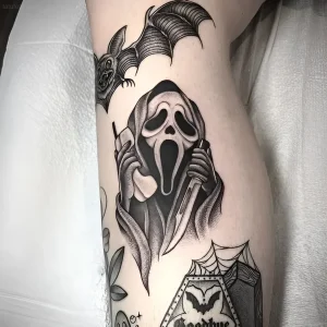 Черно-белая татуировка в стиле нео-традишн с изображением персонажа Ghostface из фильма «Крик», держащего телефон и нож, дополненная летучей мышью и паутиной