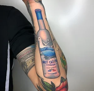 Детальная татуировка бутылки водки Grey Goose на руке в стиле реализм с голубем и французским флагом