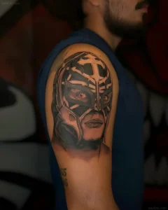 татуировка luchador на плече мужчины, реализм, черная маска с перьями, красные глаза, темная цветовая гамма