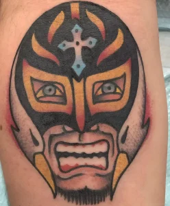 татуировка на тему борьбы с маской luchador, красно-оранжевая маска с черным контуром и голубым крестом, реализм в нижней части лица, тату на руке