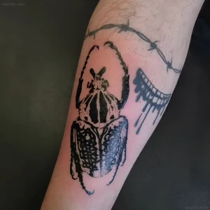 Татуировка на предплечье в стиле blackwork с изображением майского жука, колючей проволоки и капель чернил
