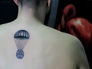 Черно-серая татуировка на спине мужчины, изображающая человеческий мозг, парящий в воздухе на парашюте