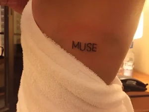 Фото татуировки с надписью MUSE на боку человека, обернутого в полотенце, в стиле минимализм