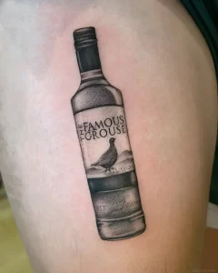Черно-белая татуировка в стиле реализм с изображением бутылки виски Famous Grouse на коже плеча