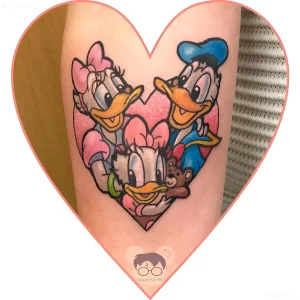 Яркая цветная татуировка с персонажами Disney — Дональдом Даком, Дейзи и Донной — в стиле Neo-Traditional, выполненная на предплечье, с сердцем на фоне и медвежонком в руках Донны