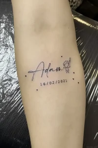 Свежая татуировка на предплечье с именем Adam, датой 16/02/2021 и силуэтом мальчика с воздушным шариком