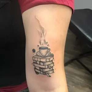 Черно-белая татуировка на предплечье: стопка старых книг с чашкой горячего кофе сверху, пар поднимается вверх, вокруг — мелкие детали в стиле дотворк