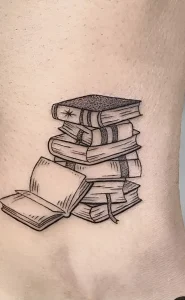 Черно-белая татуировка в виде стопки книг, одна из которых открыта, выполненная в стиле лайнворк на коже предплечья