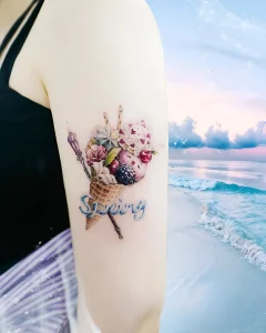 Тату на предплечье с цветным конусом мороженого, цветами и надписью Spring