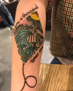 Татуировка на предплечье с изображением горы, волны и текста 'Love you a thousand times over', выполненная в стиле neo-traditional с элементами акварели и чернильной графики