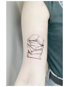 Черно-белая татуировка в стиле реализма, изображающая стопку книг на внутренней стороне предплечья, посвященная Общероссийскому дню библиотек