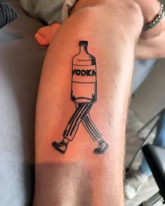 Черно-белая татуировка в стиле лайн-арт: бутылка водки с надписью VODKA, у которой вместо дна — ноги в полосатых штанах и ботинках, идущие по коже предплечья