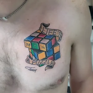 Татуировка с изображением кубика Рубика на груди мужчины с надписью LIFE'S A PUZZLE