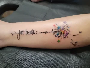 Татуировка с надписью Just breathe, стрелками и цветным одуванчиком на руке