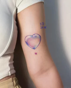 Татуировка в виде мыльного пузыря с надписью PITY SKIN на предплечье
