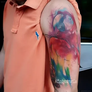Крупный план татуировки попугая в стиле watercolor на плече человека в персиковой рубашке