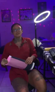 Тату-мастер Эстеффани в красном костюме с татуировками на шее и ногах в студии с фиолетовым светом