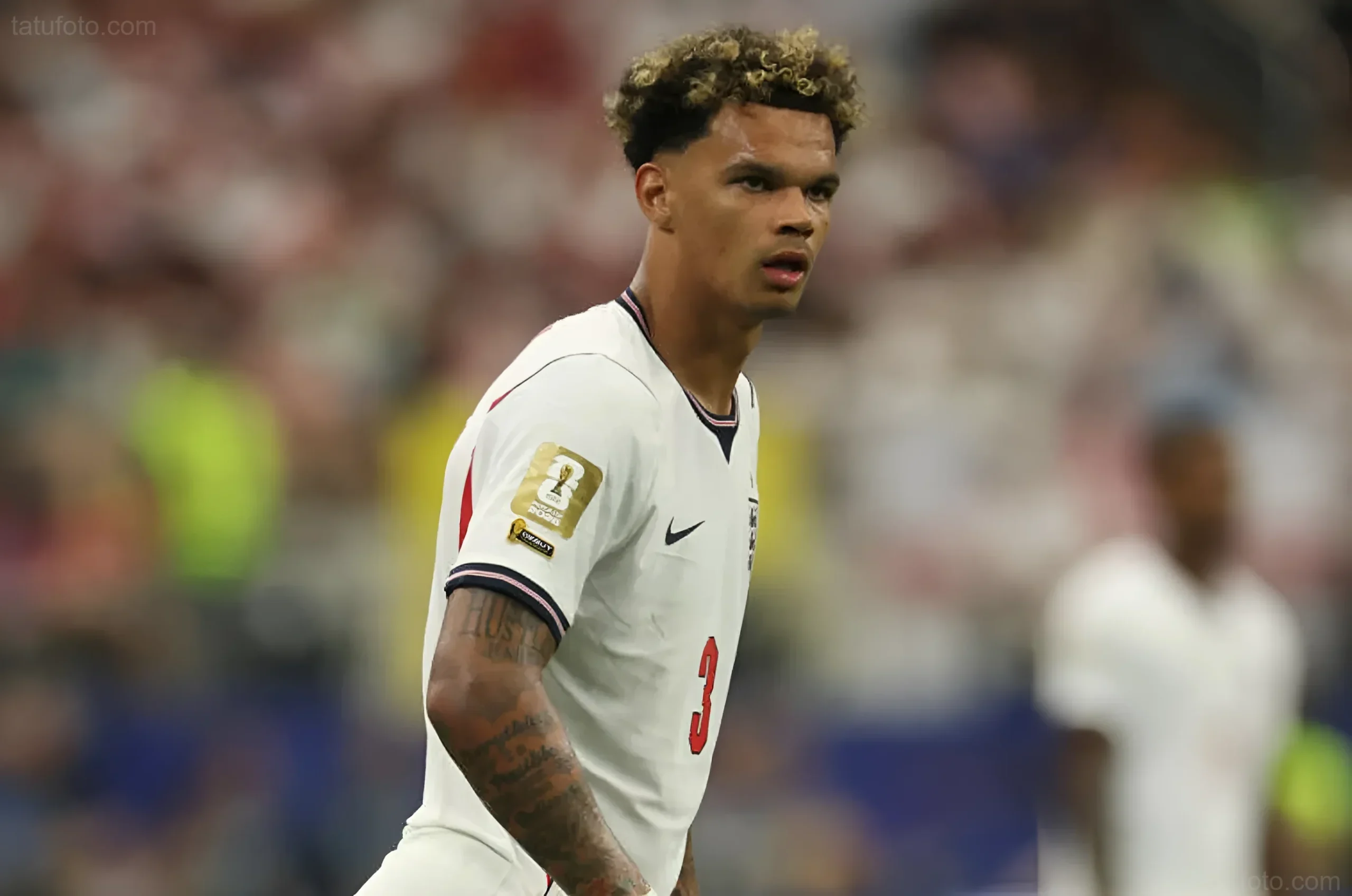 Футболист Нико О'Райли в белой форме сборной Англии во время матча, на его правой руке видны татуировки