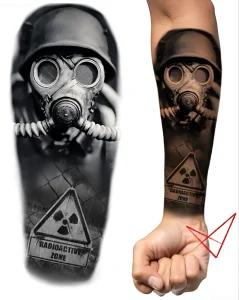 Фотография татуировки в стиле реализм на мужском предплечье с изображением лица в противогазе, шлема и знака радиационной опасности, рядом эскиз