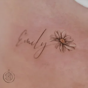 Нежная татуировка на коже с надписью Emily и цветком маргаритки, выполненная тонкими линиями в монохромном стиле