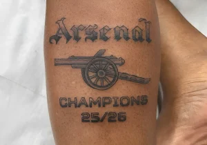 Свежая черная татуировка на предплечье с надписью Arsenal, изображением пушки и текстом Champions 25/26