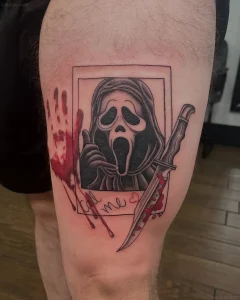 Татуировка на бедре с изображением маской Ghostface из фильма Крик, держащей палец у губ, рядом нож в крови и надпись call me, стилизованная под поляроид