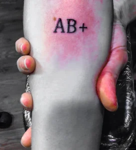 Свежая татуировка с надписью AB+ на предплечье человека, демонстрирующая актуальный тренд татуировок с группой крови