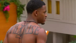 Синсер Риа из реалити-шоу Love Island USA без футболки, демонстрирующий крупную татуировку с надписью RISE на верхней части спины