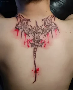 Свежая татуировка в стиле blackwork с изображением острого шипа и красных капель крови на верхней части спины человека
