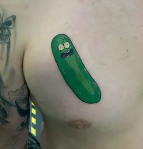 Яркая цветная татуировка персонажа Pickle Rick из мультсериала Rick and Morty на груди человека, выполненная в стиле cartoon tattoo с детализированным выражением лица и характерными шипами огурца