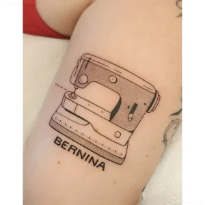 Черно-белая татуировка ретро швейной машинки Bernina на коже предплечья, выполненная в графическом стиле с минималистичными линиями