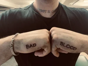 Мужские кулаки с татуировками BAD на левом и BLOOD на правом, демонстрирующими стильный минимализм в честь Всемирного дня донора крови