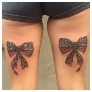 Фотография двух симметричных татуировок в виде черных кружевных бантов, расположенных на бедрах девушки. Исполнены в стиле реализм с детальной проработкой узора.