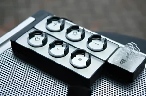 Ближний план устройства CipherX Microdot Tattoo System с набором сменных головок с символами: сердце, звезда, крест, улыбка и другие. Устройство расположено на металлической поверхности с перфорацией.