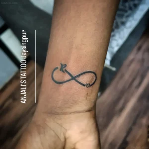Черно-белая татуировка в стиле минимализм на запястье: знак бесконечности с сердцем и буквой R