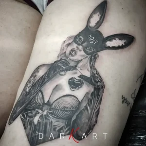 Чёрно-белая татуировка на бедре: девушка в маске кролика с надписью 'HOP', в корсете и перчатках, с сердечком на груди — стиль реализм с элементами neo-traditional