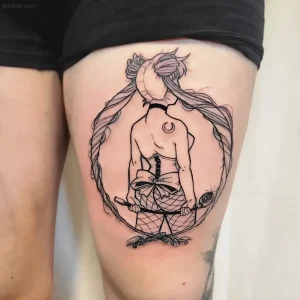 Черно-белая татуировка на бедре девушки, изображающая женскую фигуру с длинными волосами, корсетом, сетчатым бельем и плетью, в окружении круглого орнамента
