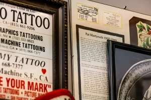 Крупный план витрины студии Picture Machine Tattoo: слева список услуг и телефонов, справа биографическая справка о владельце Пате Мартинюике и старинные визитки